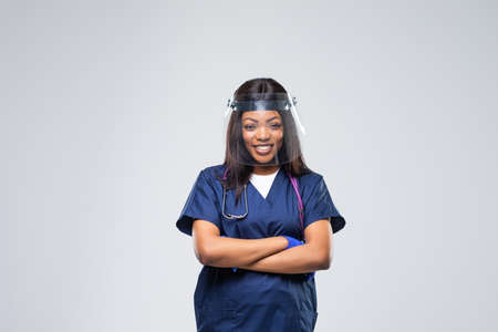 Portrait of young beautiful african female EMS medical worker, wearing uniform and protective face shield isolated on white background. Stress and worry due to Coronavirus COVID-19 pandemicの写真素材