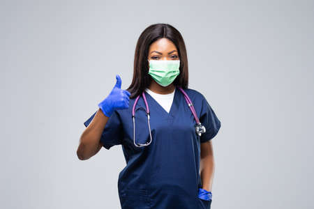 Young beautiful female doctor with protective face mask, waist up. Woman hospital worker looking at camera and smiling, studio, gray backgroundの写真素材