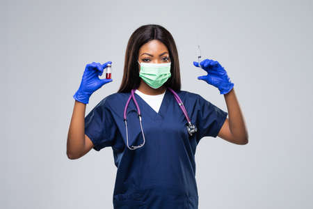 medicine, vaccination and healthcare concept - african american female doctor or scientist in mask with syringe with vaccine of COVID over gray backgroundの写真素材