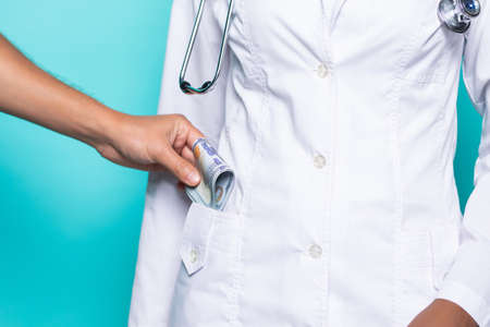 Doctor putting bribe into pocket on turqouise background, closeup.の写真素材