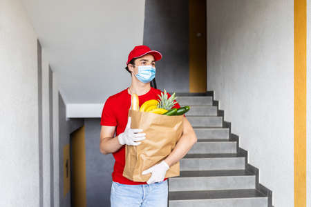 Food delivery service, male worker holding grocery bag at building, express food order