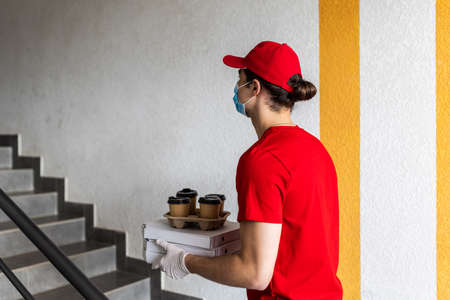 Outdoor portrait of delivery man in uniform with cardboard brown and white boxes and take away...