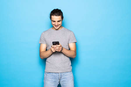 Young man posing isolated over blue wall background using mobile phone chatting.