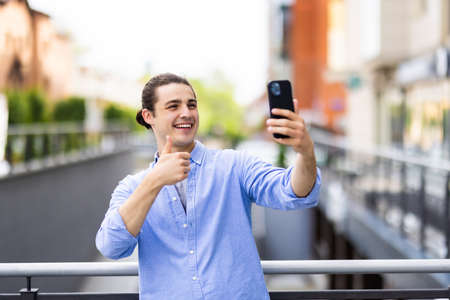 Young man holding and talking on smartphone via video call while sitting in the cityの写真素材