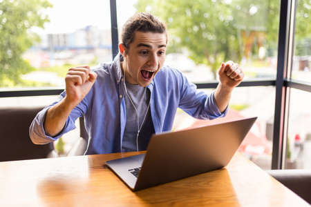 Overjoyed caucasian man celebrating victory in computer game enjoy playing on laptop computer during free time, happy male freelancer excited with completing online project successfullyの写真素材