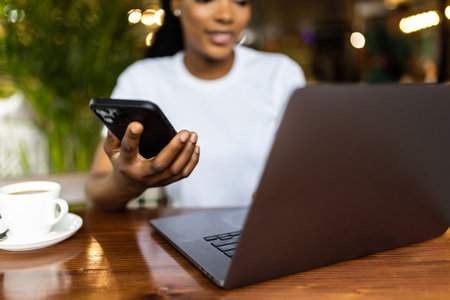 African american woman using laptop and smartphone near cup in cafe