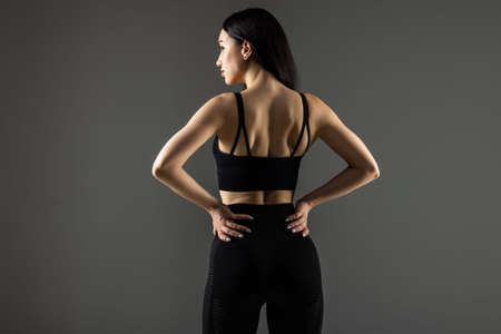 Tough young woman standing on gray background. Muscular female looking at camera. Female bodybuilder wearing gloves ready for gym exercise.の写真素材
