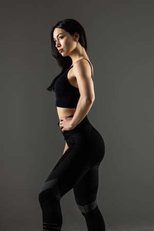 Tough young woman standing on gray background. Muscular female looking at camera. Female bodybuilder wearing gloves ready for gym exercise.の写真素材