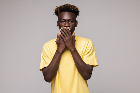 Shocked horrified african man covering mouth with hands feel scared looking at camera isolated on white backgroundの写真素材