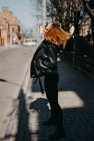 young woman walking in street in fashionable outfit, wearing black leather jacket, spring autumn style, posing, high leather bootsの写真素材