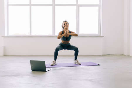 Happy positive smiling beautiful girl exercising fit mat at gym watching sportive video in laptop...