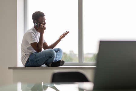 Young handsome african man in casual outfit talking on the phone in office