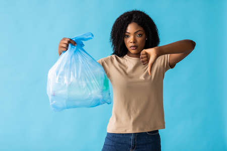 African woman holding a bag full of plastic bottles for recycling in blue backgroundの写真素材