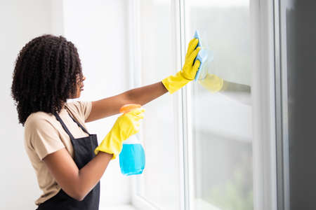 Smiling afro american woman cleaning glass window at houseの写真素材