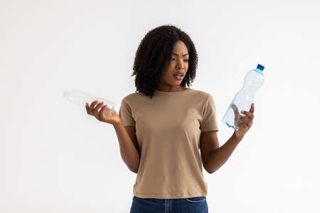 Surprised african-american girl holding plastic bottles for recycling isolated over white backgroundの写真素材