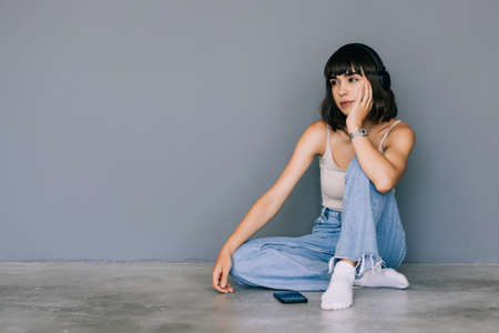 Smiling young womansitting on a floor with legs crossed looking up on gray backgroundの写真素材