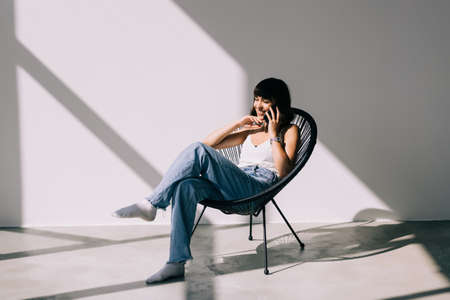 Beautiful young woman sitting on a chair and talking at phoneの写真素材
