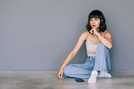 Smiling young womansitting on a floor with legs crossed looking up on gray backgroundの写真素材