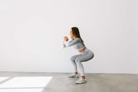 Portrait of a confident fitness woman doing squats isolated over white backgroundの写真素材