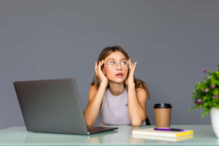 Young woman at modern office desk, working on laptop, massaging temples to forget about constant headaches, noisy loud office giving a migraine, relieving stress, chronic pain, help sootheの写真素材