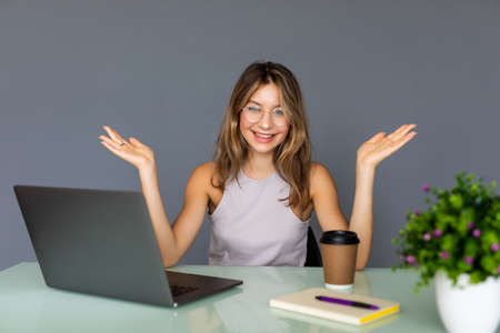 Cheerful young woman in glasses looking at camera with smile while sitting at her working placeの写真素材