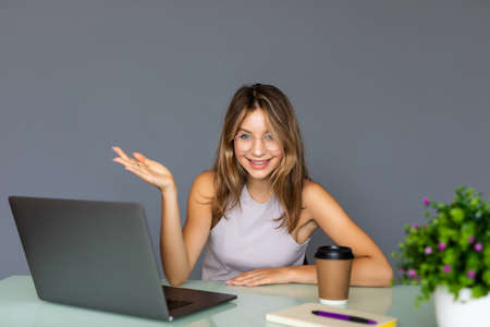 Cheerful young woman in glasses looking at camera with smile while sitting at her working place