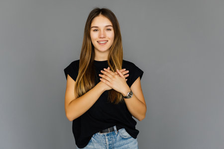 Young woman on the gray background in casual smart beige outfit is touch a heart symbol with her handsの写真素材