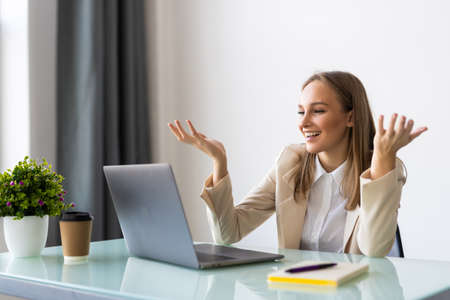 Attractive mad businesswoman in white blouse sitting at her workplace in office, looking at laptop...