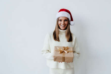 Woman in Santa hat holding gifts on white background