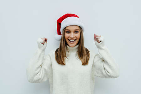 Young beautiful woman wearing a Santa hat over white background very happy and excited making winner gesture with raised arms, smiling and screaming for success.の写真素材