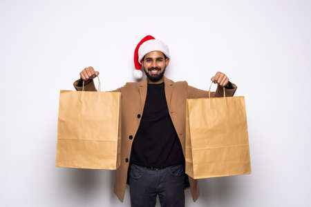 Young man in santa hat holding shopping bags while looking away on white backgroundの写真素材