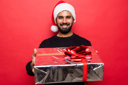 Young handsome man enjoying christmas time with presents on red backgroundの写真素材