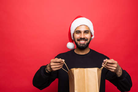Young handsome man in santa hat holding shopping bag on red backgroundの写真素材