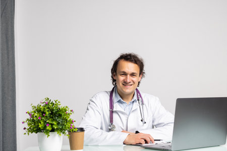medicine, profession, technology and people concept - smiling male doctor with laptop in medical officeの写真素材