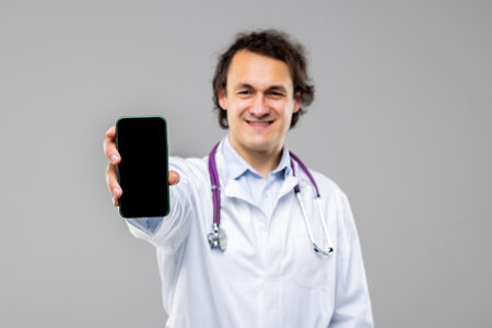 Doctor presenting smart phone and pointing blank black screen with copyspace for ads on white background,の写真素材