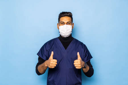 handsome young Indian Asian doctor with stethoscope in white coat showing thumb up on blue background.の写真素材