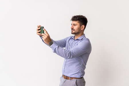 Young casual man holding cellphone taking photo isolated over white studio background.の写真素材