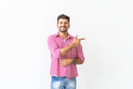 Look over there. Happy young handsome man in jeans shirt pointing away and smiling while standing against white backgroundの写真素材