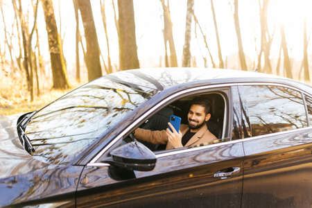 Driver taking photo with camera smartphone driving in car. Happy man taking picture with phone camera out window of car during travel road trip.の写真素材