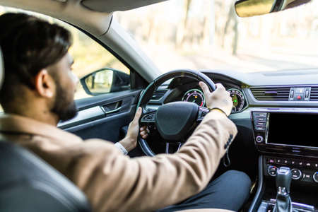 Success in motion. Handsome young man in full suit smiling while driving a carの写真素材