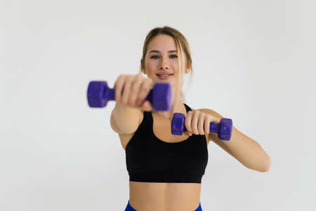 Muscular woman doing exercises with dumbbells at biceps on white background