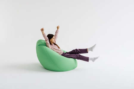 Teen girl lying down with raised hands on beanbag isolated on white background.の写真素材