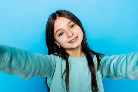 Portrait of friendly caucasian little girl over blue background taking selfieの写真素材