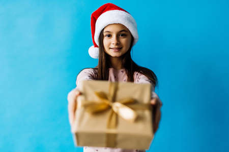 christmas, holidays and people concept - happy smiling teenage girl in santa helper hat holding gift...