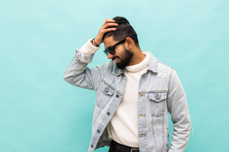 Photo of confident cheerful handsome indian man summer vacation wear sunglass green hoodie isolated teal color backgroundの写真素材