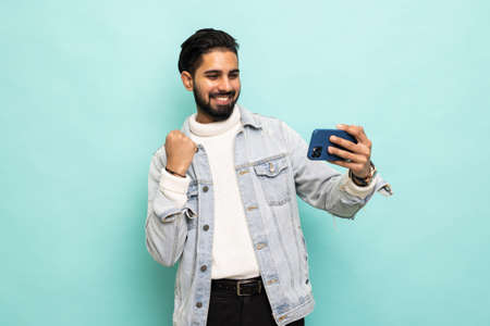 Portrait of funky astonished man hold mobile phone scream goal on teal backgroundの写真素材