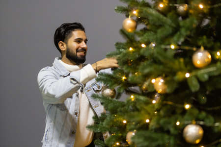 Excited amazed man in santa claus hat decorating new year tree evergreen at home