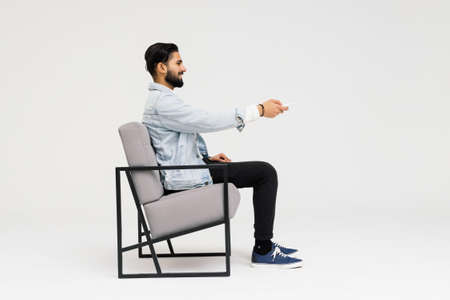 Side view of Asian man sitting in the armchair while watching TV in the studioの写真素材