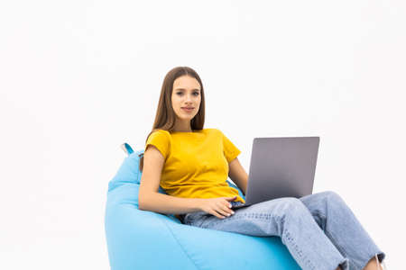 Young female sitting on a bean bag chair and using a laptop isolated on white backgroundの写真素材