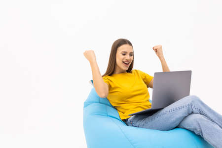 Full length photo portrait of cheerful woman with laptop sitting in beanbag on white backgroundの写真素材